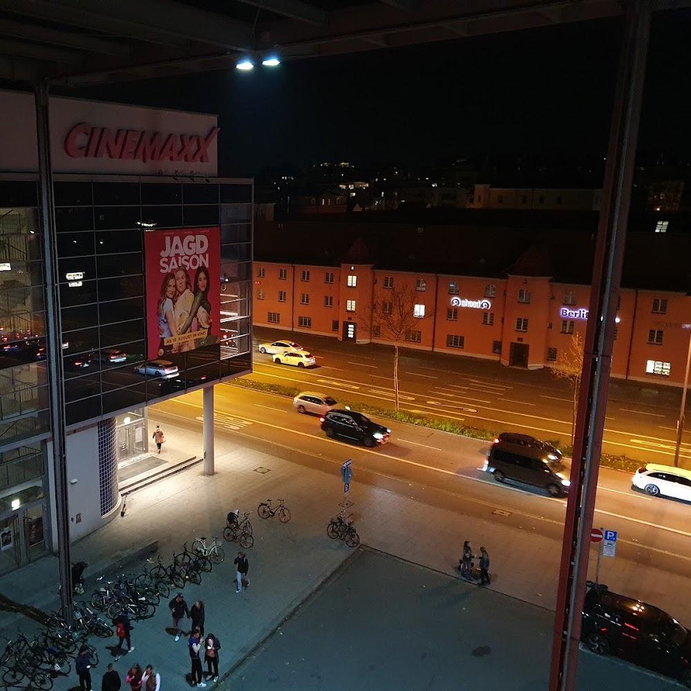 A night view of a street with a cinema building, people, and cars. The building has a sign that reads